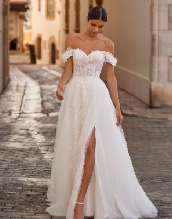 A woman in a white wedding dress is standing on a cobblestone street.