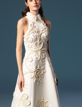 A woman in a white dress is standing in front of a blue background.