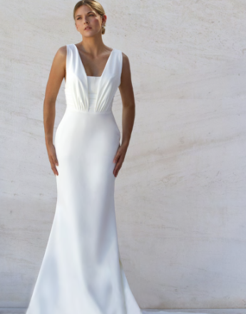 A woman in a white dress is standing in front of a white wall.