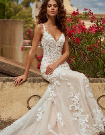 A woman in a wedding dress is sitting on a wall.