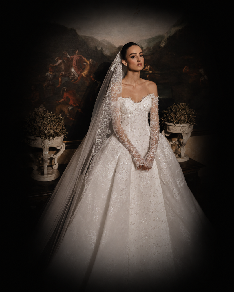 Bride in a sparkling white gown and veil stands before a dark floral backdrop.