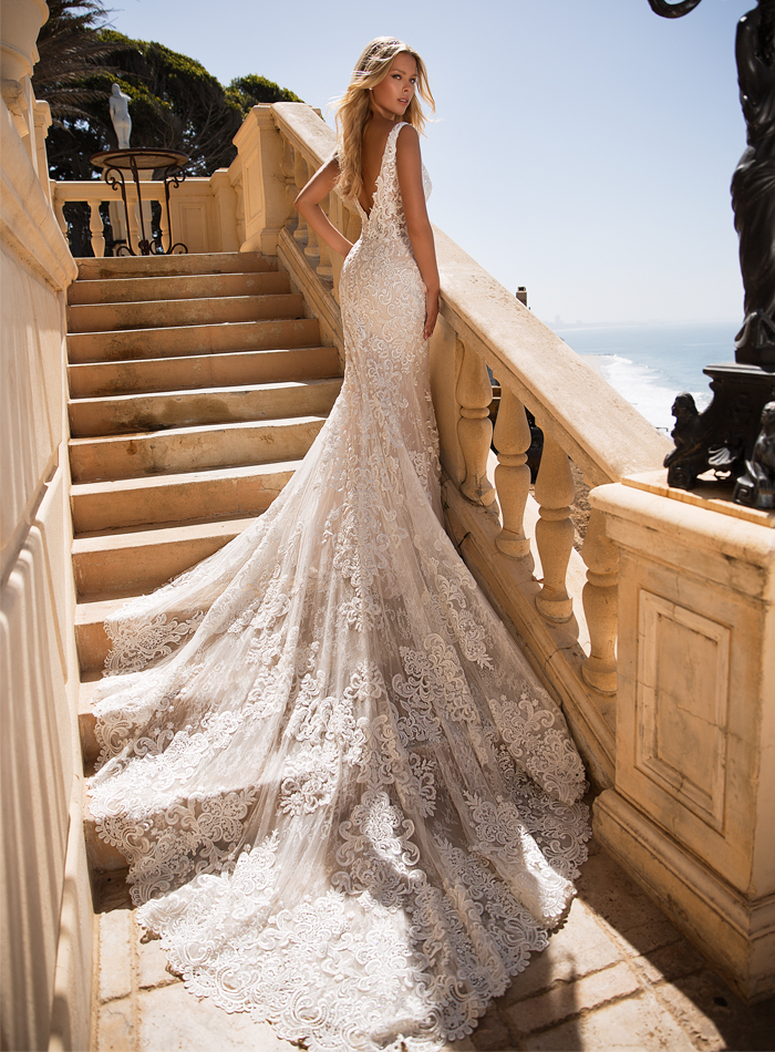 Woman in a white lace wedding gown on a stone staircase overlooking the ocean.