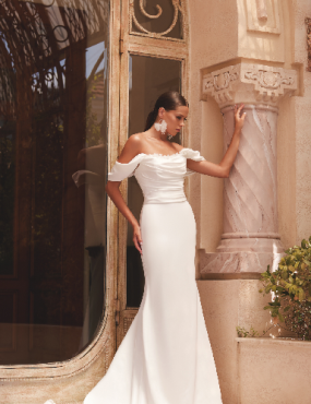 A woman in a white dress is standing in front of a building.