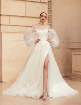 A woman in a white wedding dress with puffed sleeves is standing in front of a building.