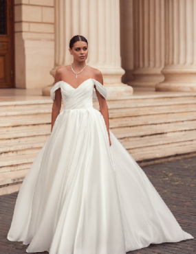 A woman in a white wedding dress is standing in front of a building.