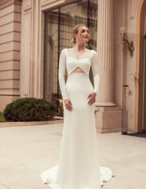 A woman in a white dress is standing in front of a building.