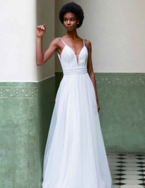 A woman in a white dress is leaning against a wall