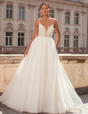 A woman in a white wedding dress is standing in front of a building.
