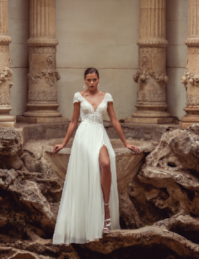 A woman in a white dress is standing in front of a fountain.