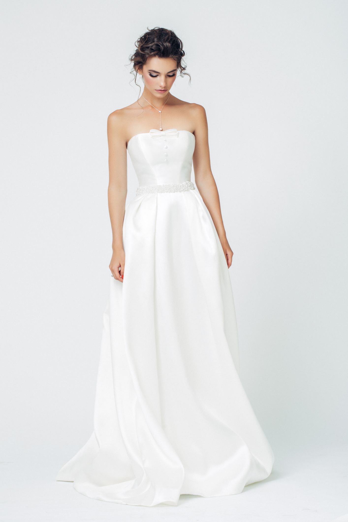 A woman in a white wedding dress is standing on a white background.