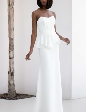 A woman in a white dress is standing next to a tree