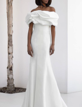 A woman in a long white dress is standing next to a tree