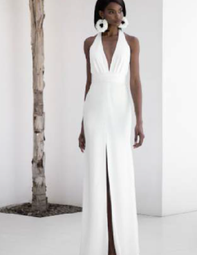 A woman in a white dress and earrings is standing next to a tree.