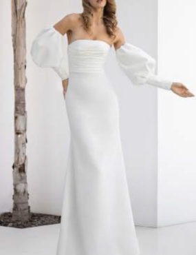 A woman in a white dress with balloon sleeves is standing next to a tree.