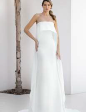 A woman in a white wedding dress is standing in front of a tree.