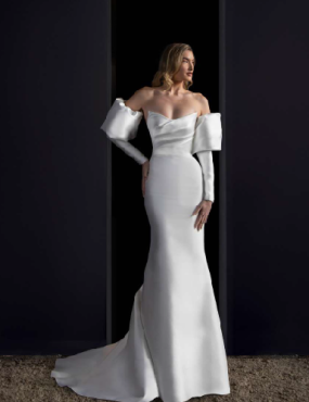 A woman in a white dress is standing in front of a black wall.