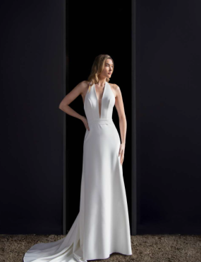 A woman in a white dress is standing in front of a black wall.