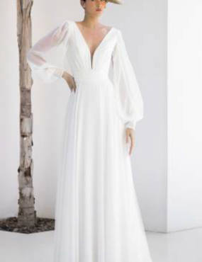 A woman in a white dress and hat is standing next to a tree.