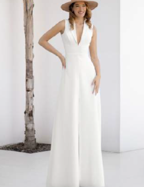 A woman wearing a white jumpsuit and a hat is standing next to a tree.