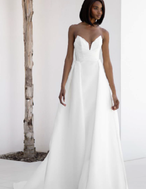 A woman in a white dress is standing next to a tree