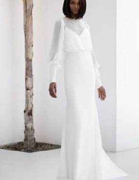 A woman in a white dress is standing next to a tree.