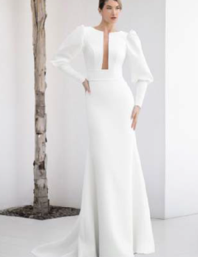 A woman in a white dress is standing in front of a tree.