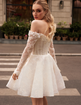 A woman is wearing a short wedding dress with long sleeves.