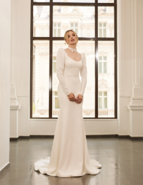 A woman in a white dress is standing in front of a window.