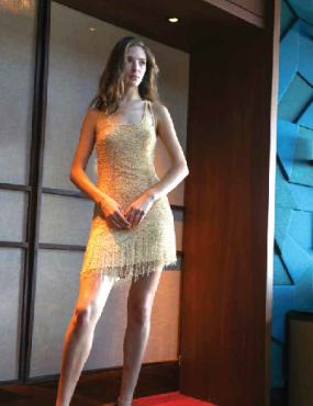 A woman in a yellow dress is standing in front of a blue wall.