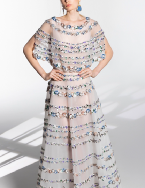 A woman in a long white dress with blue earrings is standing with her hands on her hips.