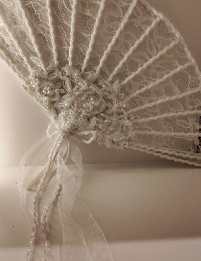 A white lace fan is sitting on a white table.
