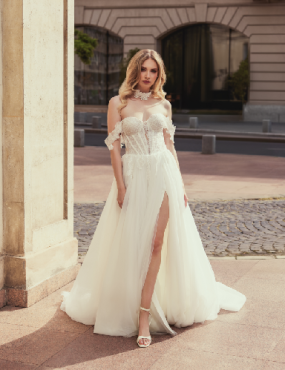 A woman in a white wedding dress with a high slit is standing in front of a building.