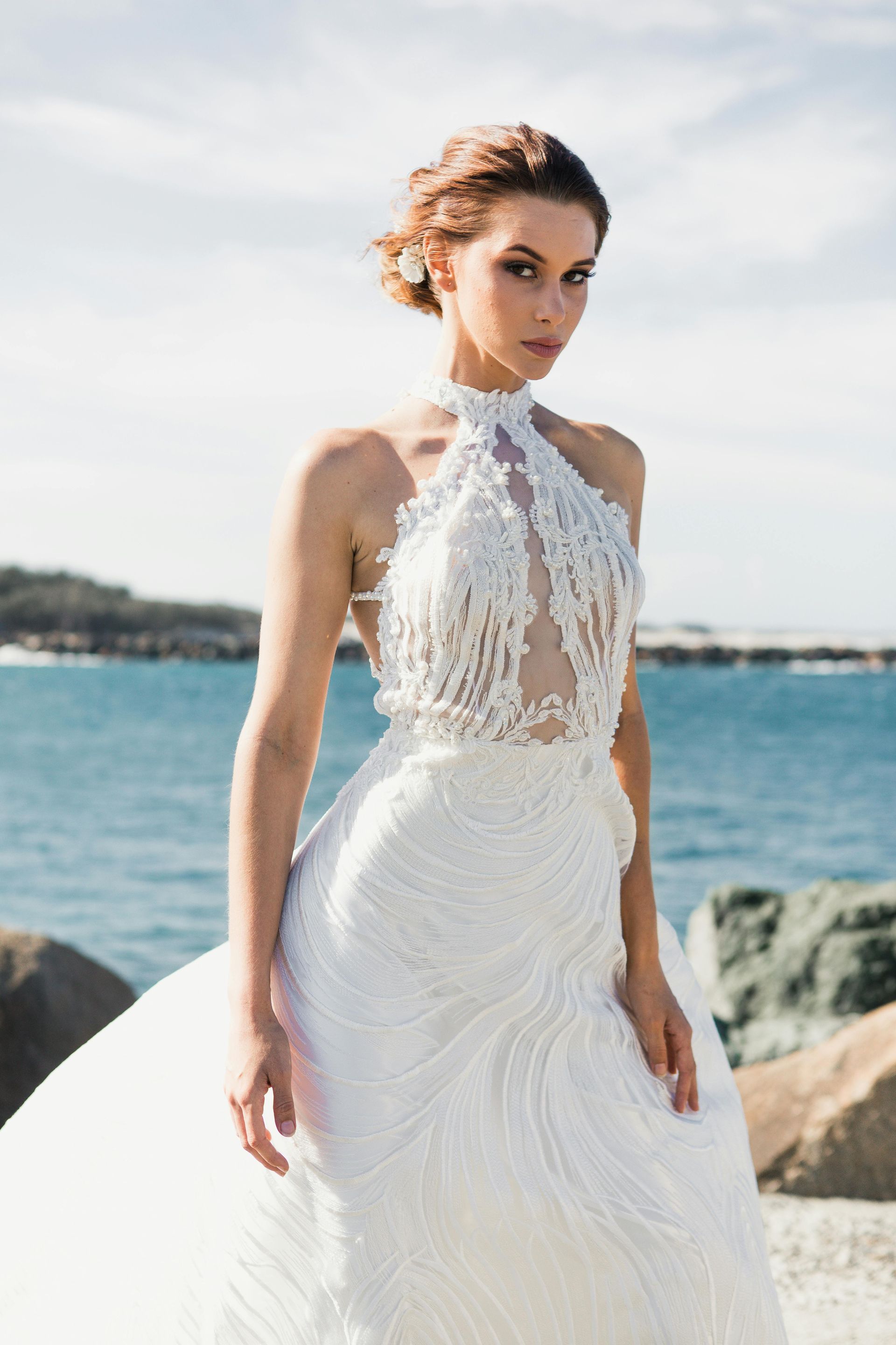 A woman in a white wedding dress is standing on a beach.