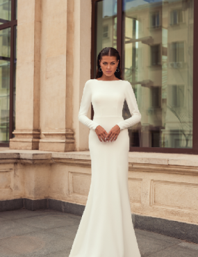 A woman in a white wedding dress is standing in front of a building.
