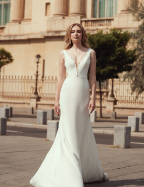 A woman in a white wedding dress is standing in front of a building.