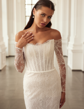 A woman is wearing a white lace wedding dress with long sleeves.