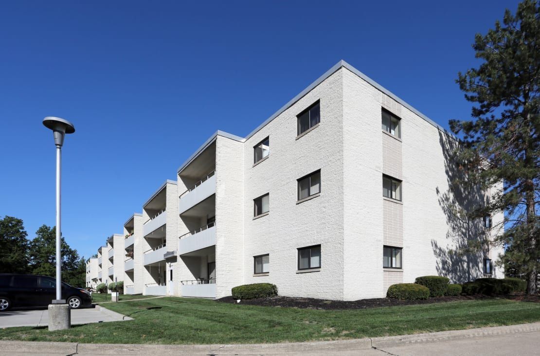 A large white apartment building with a car parked in front of it.