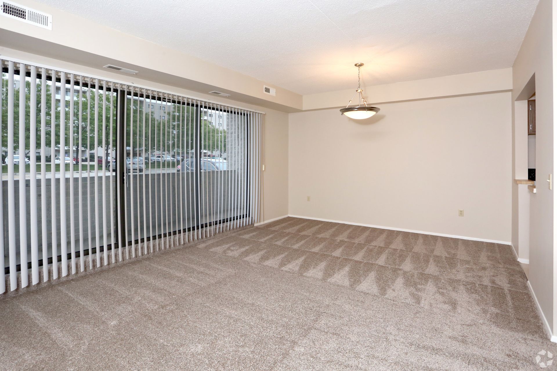 An empty living room with sliding glass doors and vertical blinds