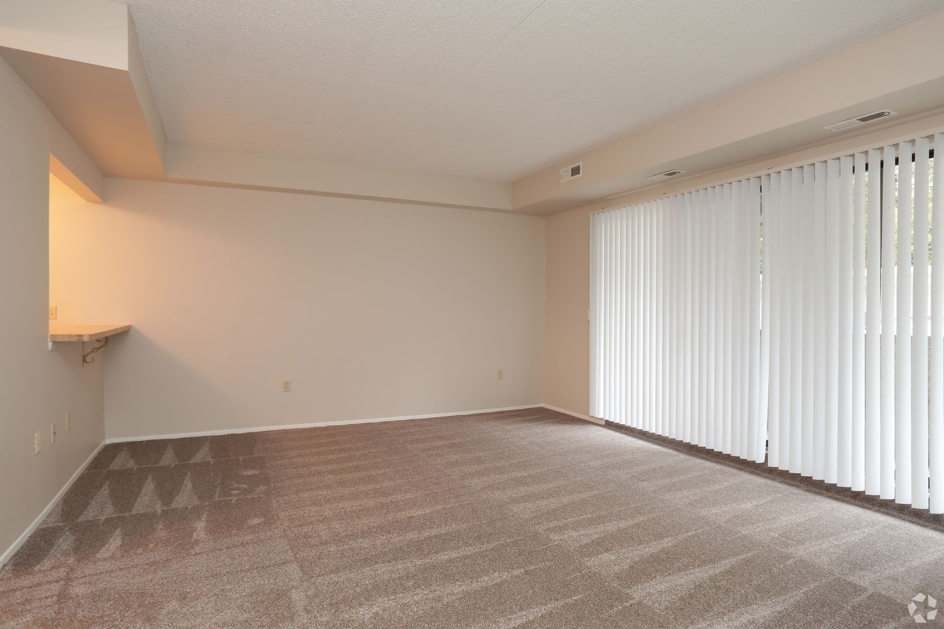 An empty living room with a sliding glass door and blinds.