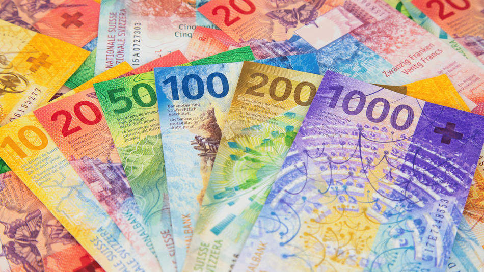 Une personne tenant un portefeuille noir ouvert, contenant de l'argent liquide et des cartes de crédit, près d'une fenêtre.