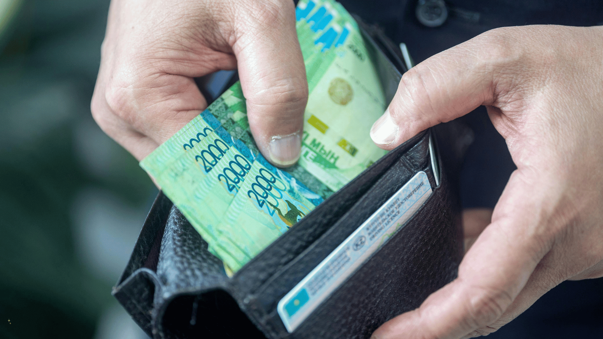 Une personne tenant un portefeuille noir ouvert, contenant de l'argent liquide et des cartes de crédit, près d'une fenêtre.