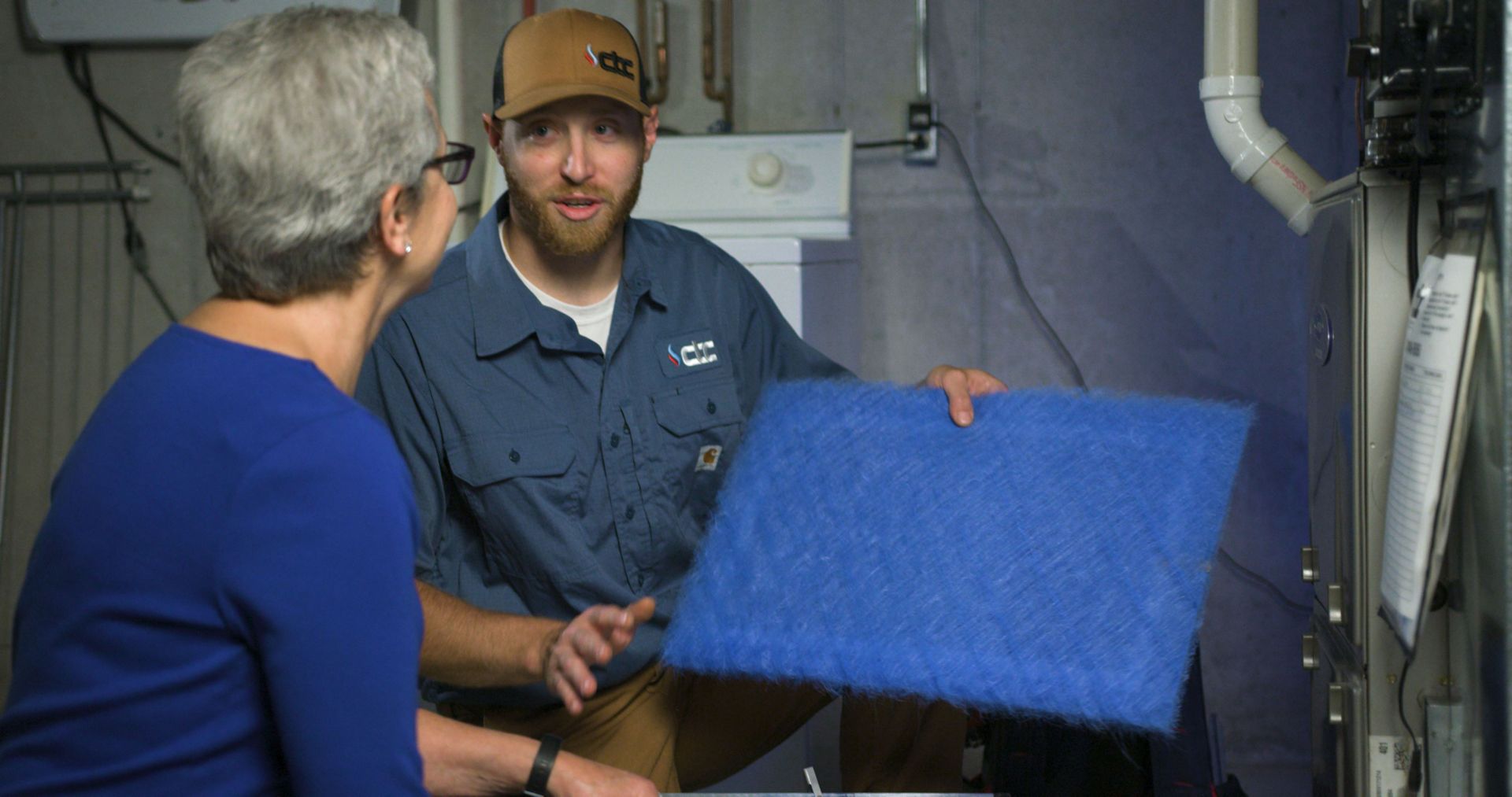 service technician explaining to a customer how to change the filter of a furnace.