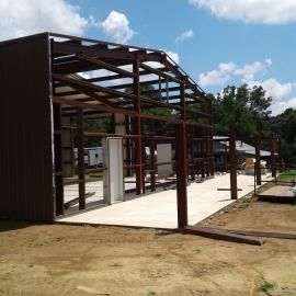 A partially constructed metal frame building on a concrete slab under a partly cloudy sky.