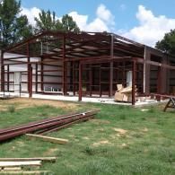 A steel frame building under construction in a grassy field with construction materials on the ground.