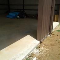 Concrete ramp entrance leading into an empty metal warehouse building with brown metal siding.