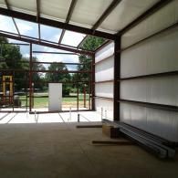 Interior view of an unfinished metal building with exposed steel framing, concrete flooring, and white insulation.