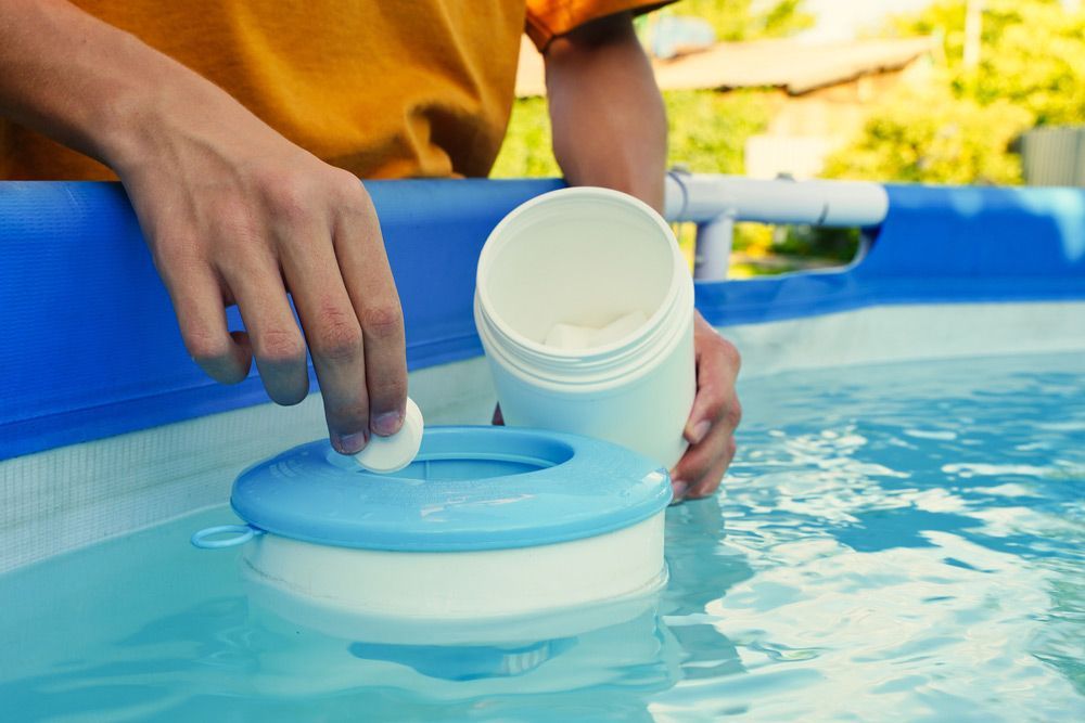 Hand Holding White Chlorine Tablets Over Swimming Pool Skimmer — Professional Pool Builder in Wagga Wagga, NSW