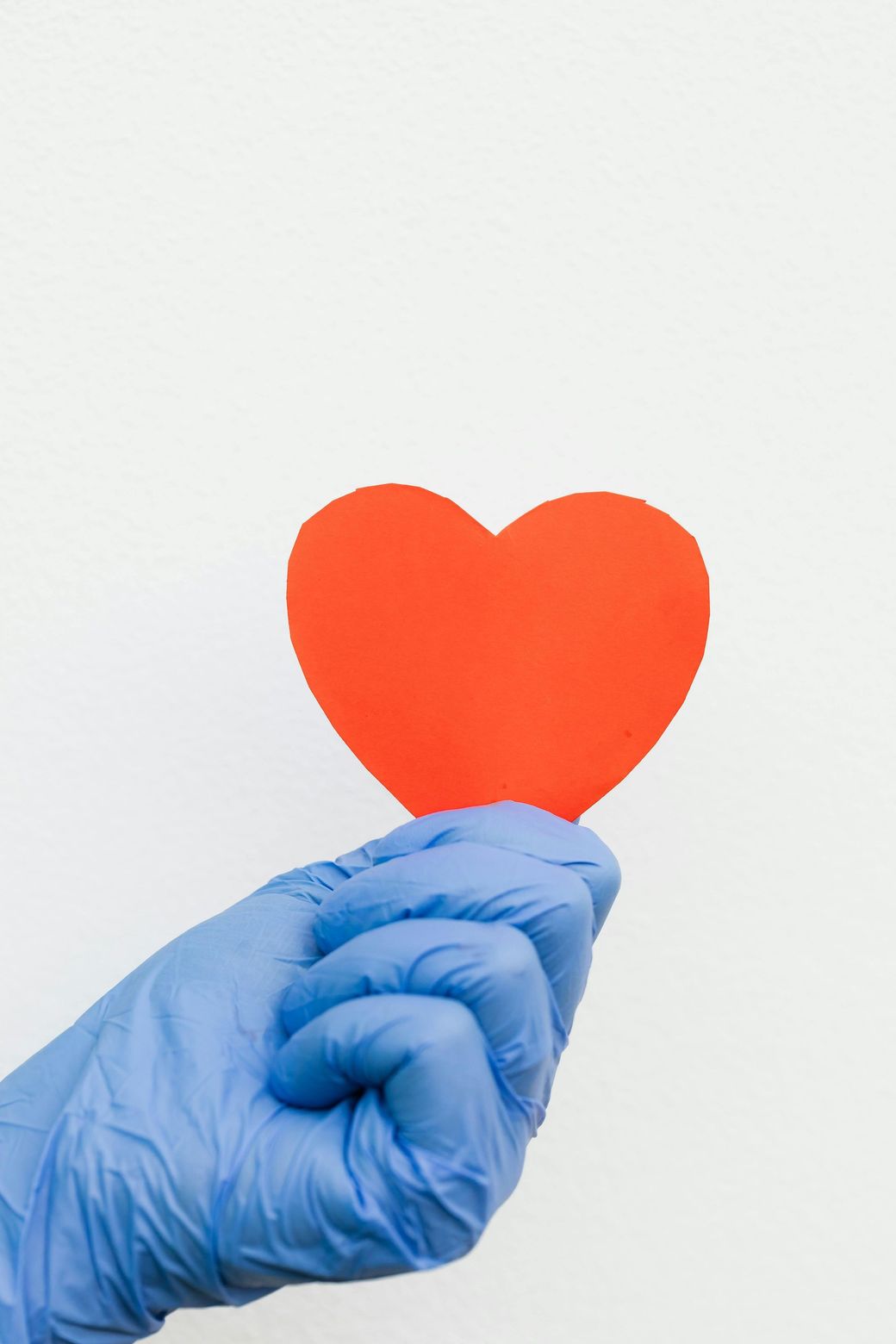 Paper cutout heart held by hand by a medical professional in a medical sterile glove.