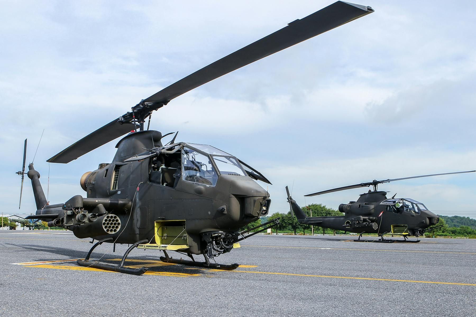 Two black military attack helicopters on a gray tarmac against a cloudy sky.