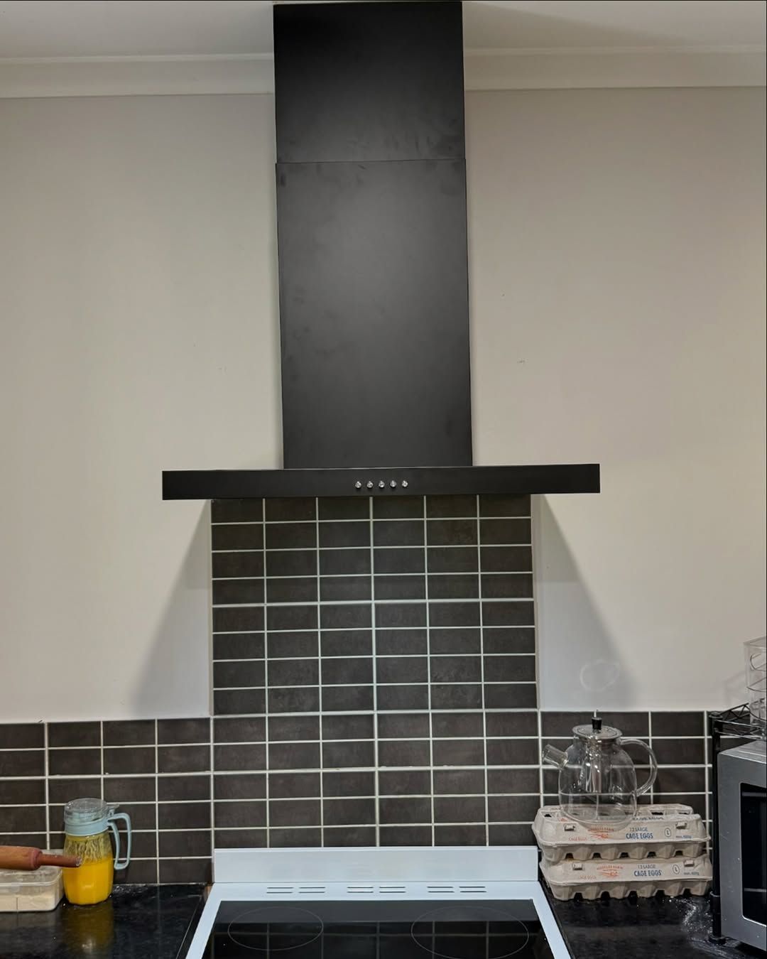 Modern black rangehood with tiled splashback in kitchen.